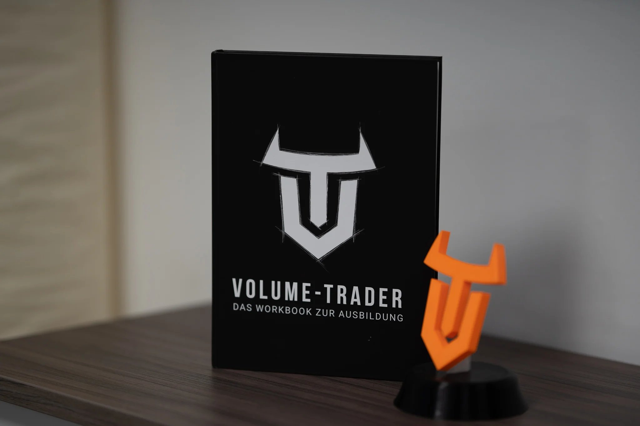 Nahaufnahme eines Buches, auf welchem "Volume-Trader Das Workbook zur Ausbildung" geschrieben steht. Daneben das Logo in Plastik